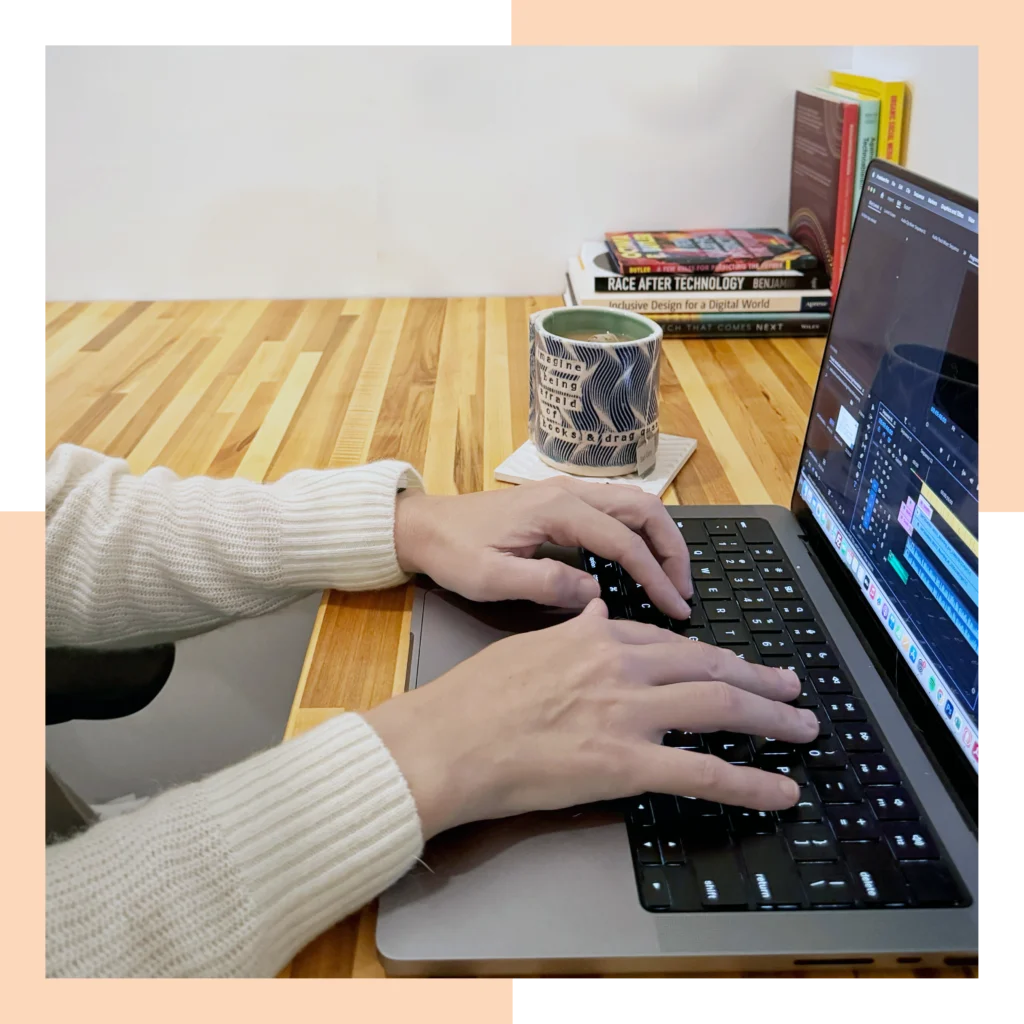 Hands typing on a laptop at a desk. There' also a cup of tea and books on the desk.